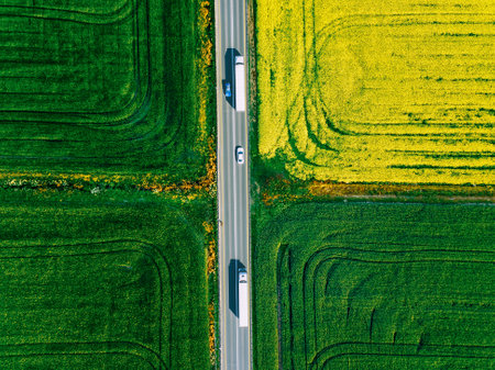 Aerial view of white trucks and cars driving on asphalt road along the green and yellow fields in Finland. Cargo delivery logistic concept.の写真素材