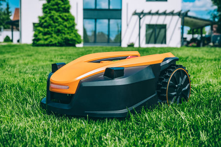 Automatic robotic lawn mower on a green lawn with modern house in background. Grass lawn mower robot in sunny summer day.の写真素材