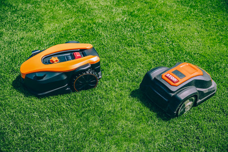 Two Automatic robotic lawn mowers on a green lawn. Robotic lawn mower on a sunny summer day.の写真素材