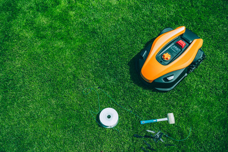 Ready to lays a cable and hammers in a plastic peg for autonomous operation of a robotic lawn mower. Roll of wire for robotic lawn mower, plastic pegs, connectors and robot.の写真素材