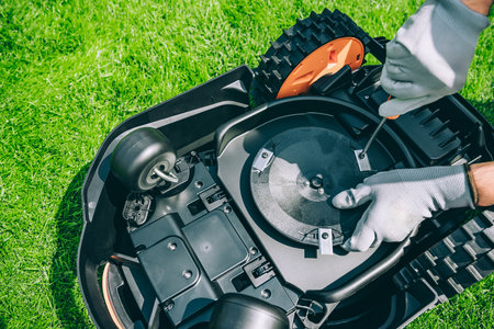 A man changes the blades of a robotic lawn mower. Lawn Mower Maintenance at Home Workshop With Tools on a Sunny Dayの写真素材