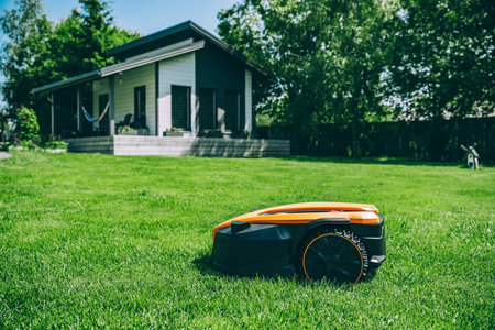 Automatic robotic lawn mower on a green lawn with cozy house in background. Grass lawn mower robot in sunny summer day.の写真素材