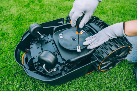 A man changes the blades of a robotic lawn mower. Lawn Mower Maintenance at Home Workshop With Tools on a Sunny Dayの写真素材