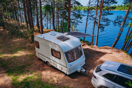 Aerial view of Caravan RV parked on the beach under a trees facing blue sea, lake or river. Family...