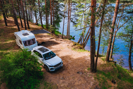 Aerial view of Caravan RV parked on the beach under a trees facing blue sea, lake or river. Family traveling with motorhome. Travelers on an active family vacation.の写真素材