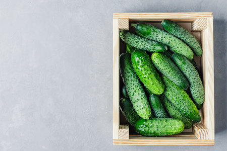 Crate full of cucumbers. The crate is wooden and the cucumbers are green. The crate is on a gray surfaceの写真素材