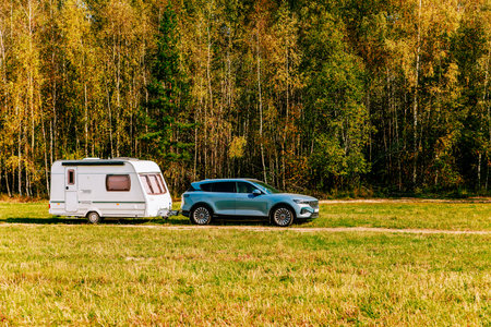 Camping caravan rv in autumn fall landscape. Caravan trailer in a golden tree forest. Colorful red,...