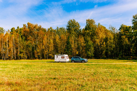 Camping caravan rv in autumn fall landscape. Caravan trailer in a golden tree forest. Colorful red,...