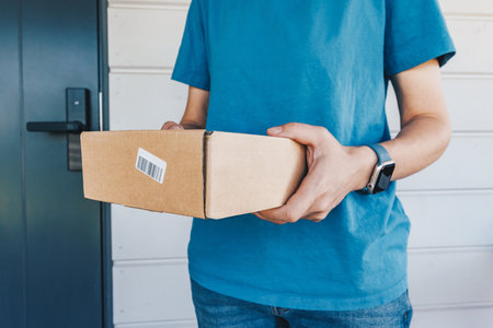 A delivery worker in a blue uniform holds boxes of parcels at a customer's door. Concept for...