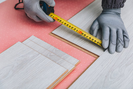 Measuring Wood Panels with a Tape Measure while Installing Flooring Materials for a Home Renovation...