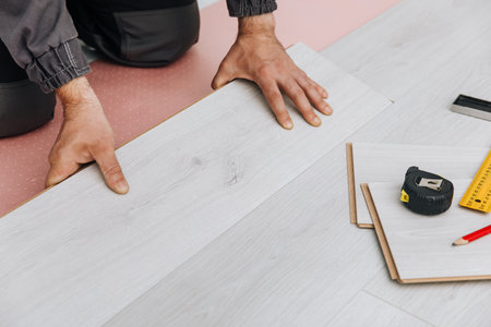 A Person Installing Laminated Flooring in a Room with Tools and Materials for Home Renovationの写真素材