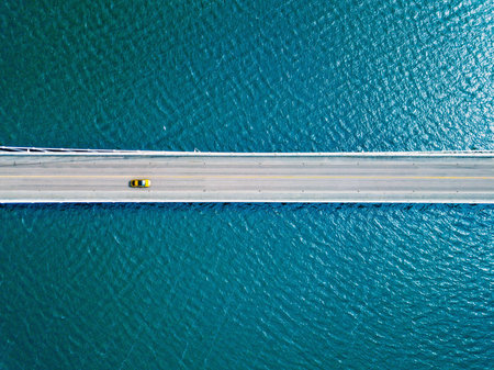 Aerial View of a Colorful Vehicle Crossing a Bridge Over Serene Blue Water