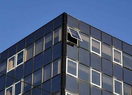 Modern building with open and closed windows against blue sky