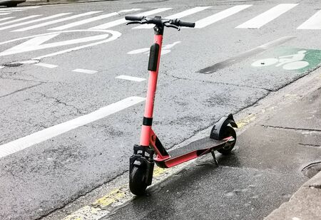Red color rental electric scooter on the sidewalk