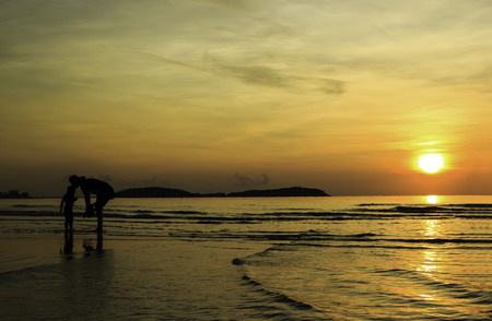 Silhouette of mother and son playing water at sunriseの写真素材