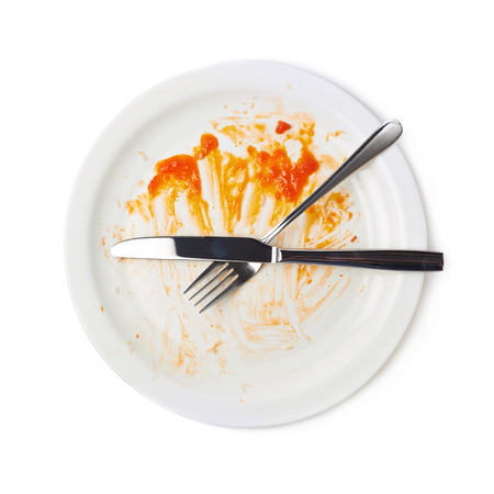 Orange sauce food leftovers in a white ceramic plate, knife and fork over it, composition isolated over the white backgroundの写真素材