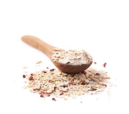 Pile of oatmeal porridge groats mixed with dried fruit pieces and wooden spoon over it, composition isolated over the white backgroundの写真素材
