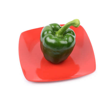 Green bell pepper on a red ceramic plate isolated over the white backgroundの写真素材