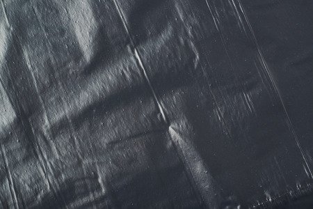 Close-up fragment of a black polyethylene trash bag's surface as a backdrop texture composition