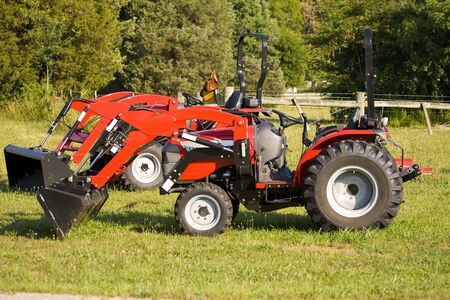 A pair of small red tractors on an agrecultural lot for sale