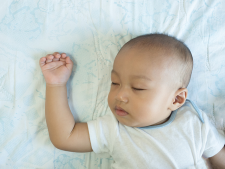 Sleeping baby on back on white bedの写真素材