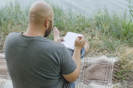 the young guy writes in a notebook in the open airの写真素材