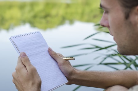 the young guy writes down in a notebook outdoors