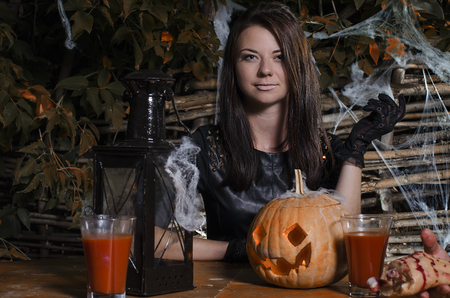 the girl the witch at a table in a suit for Halloween with pumpkinの写真素材