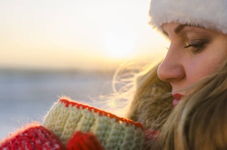 woman in red mittens holding a cup of tea at sunset