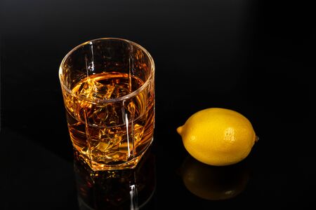 glass of whiskey with lemon on a black table with reflection