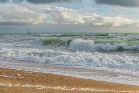 Powerful ocean waves sweep onto a sandy shore, creating white foam against a backdrop of dramatic...