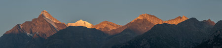 Summits of mountains light up with soft orange light while sun sets, creating spectacular panorama....