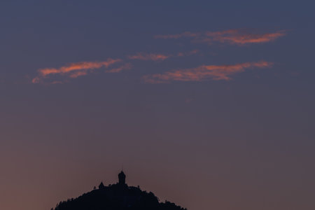 Quiet landscape shows castle perched on hill. Sky is tinged with pastel colors to twilight, offering...