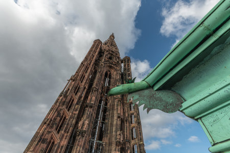 Strasbourg's Gothic cathedral stands majestically under cloudy sky. Ornate and detailed iron gargoyle is visible in foreground, adding unique charm to scene. Bas Rhin, Alsace, France, Europe.の写真素材