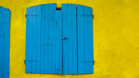 Old blue window made of wood in bright yellow wallの写真素材