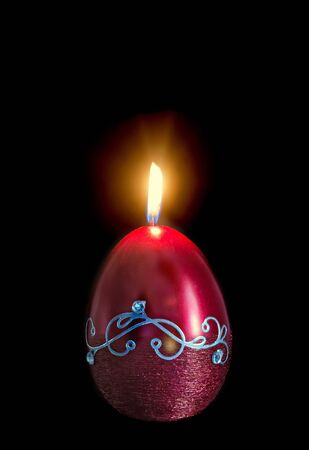 Egg shape, oval Easter candle, flame, isolated, close up, dark background.の写真素材