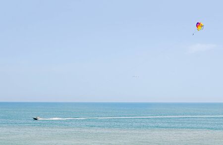 Colored parasail wing in the blue sky, Parasailing also known as parascending or parakiting. Ship on waterの写真素材