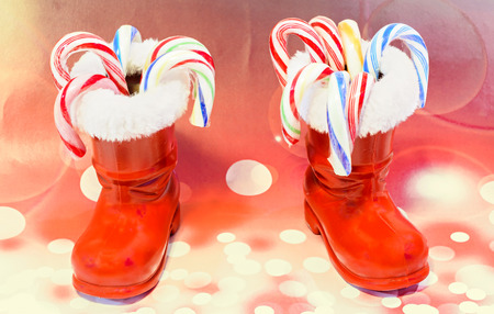 Red Santa Claus boots with candies, lollipops, shoes. Saint Nicholas boots gifts, red lights bokeh background.の写真素材
