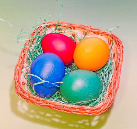 Vibrant colored easter eggs in a brown basket, gradient background, close up.の写真素材