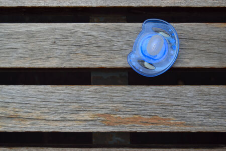 Blue pacifier on a wooden lat of a benchの写真素材
