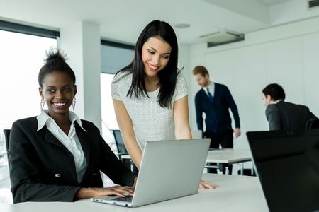 Black and white businesswomen looking at a aptop and working in a neat office environmentの写真素材