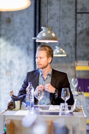Businessman buttoning shirt in a restaurant while sitting at the table with hanging lampsの写真素材