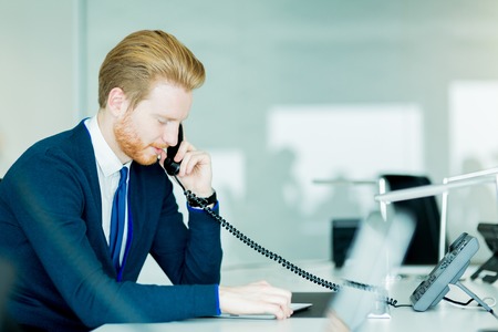 A handsome male, red haired worker in a call center office talking on a phoneの写真素材