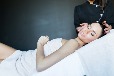 Masseur treating face of a beautiful, young woman lying on the massage tableの写真素材