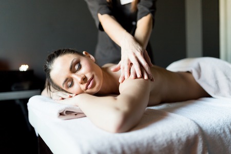Beautiful, young and healty woman having her shoulder and body massaged by a professional masseur at a spa centerの写真素材