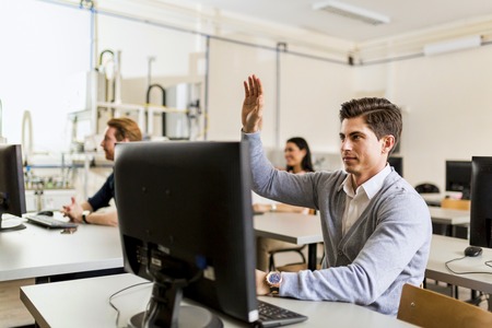 Young handsome man sitting in front of a pc raising handの写真素材