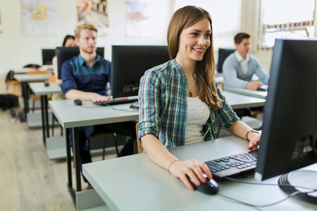 Young beautiful girl working on a computer in a classroom with her classmates in the background