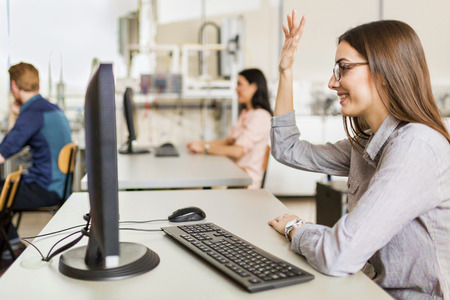 Beautiful young girl raising hand in classroom while sitting at a desk