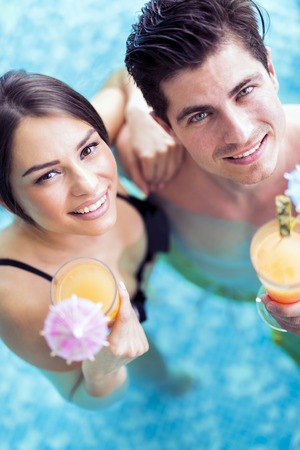 Portrait of a beautiful young couple smiling and drinking a cocktail in a poolの写真素材
