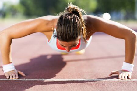 Focused young beautiful woman doing push-ups outdoors on a hot summer day